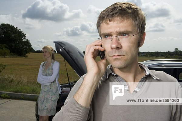 A couple standing at the roadside next to their broken down car