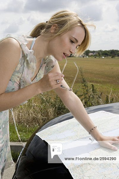 A woman leaning on a car bonnet and reading a map