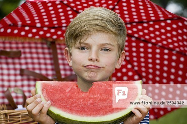 Ein Junge hält ein Stück Wassermelone mit einem fehlenden Biss.