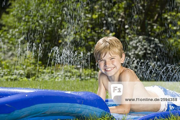 Ein Junge  der auf einer Wasserrutsche liegt.
