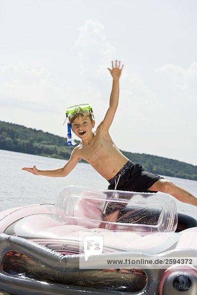 Ein kleiner Junge steht in einem Schlauchboot auf einem See.