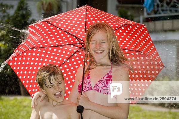 Zwei Kinder  die unter einem Regenschirm stehen und vom Spritzwasser getroffen werden.