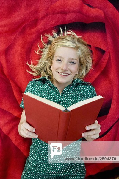 Ein Mädchen  das auf einer Decke liegt und ein Buch liest.
