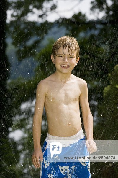 Ein kleiner Junge steht in einer Sprinkleranlage.
