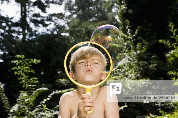 Ein Junge  der eine Blase mit einem Blasenstab bläst.