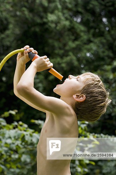 Ein kleiner Junge fängt den letzten Tropfen Wasser aus einem Gartenschlauch.