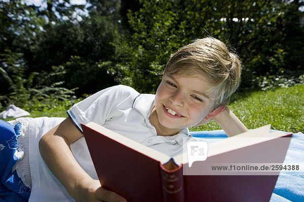 Ein Junge  der auf einer Decke liegt und ein Buch liest.