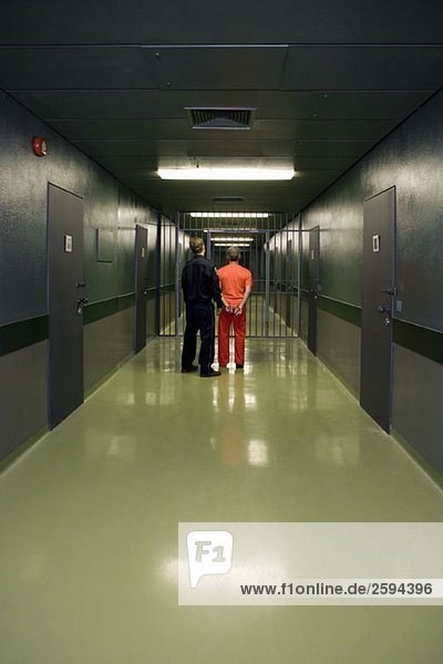 Ein Gefängniswärter  der einen Gefangenen durch einen Korridor führt.
