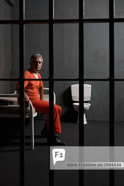 Gefangener  der auf einem Bett in einer Gefängniszelle sitzt.