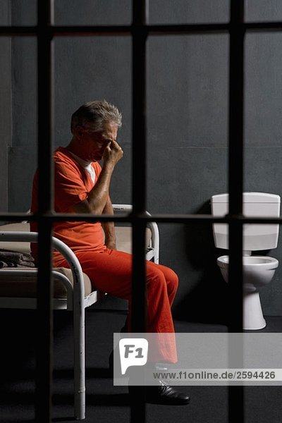 Ein Gefangener  der auf einem Bett in einer Gefängniszelle sitzt.