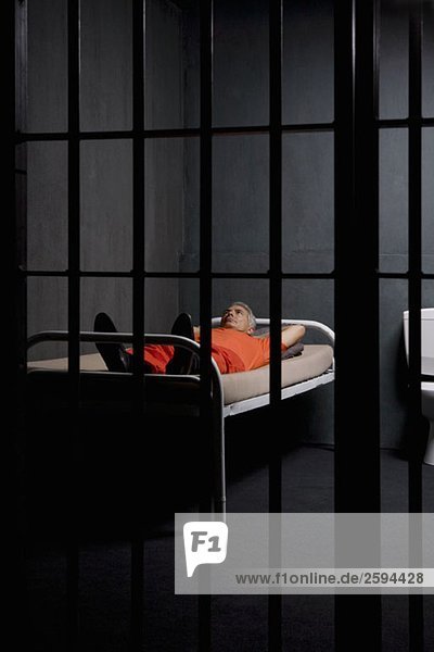 Ein Gefangener  der auf seinem Bett in einer Gefängniszelle liegt.