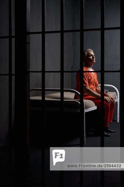 Ein Gefangener  der auf einem Bett in einer Gefängniszelle sitzt.