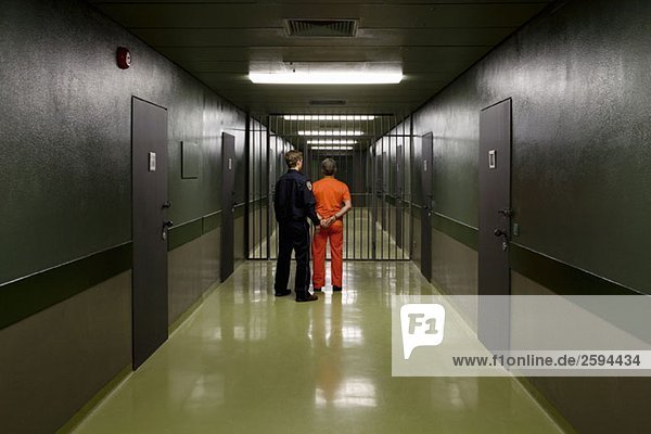 Ein Gefängniswärter  der einen Gefangenen durch einen Korridor führt.