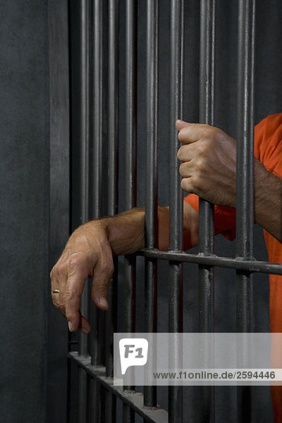 Ein Gefangener  der hinter seinen Zellengittern steht.