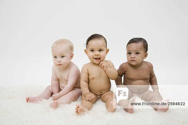 Drei nackte Babys sitzen in einer Reihe.