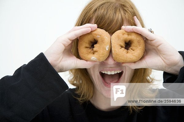 Eine Frau  die zwei Donuts vor die Augen hält.