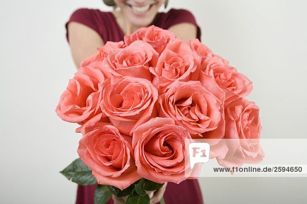 Eine lateinamerikanische Frau präsentiert einen Strauß Rosen.