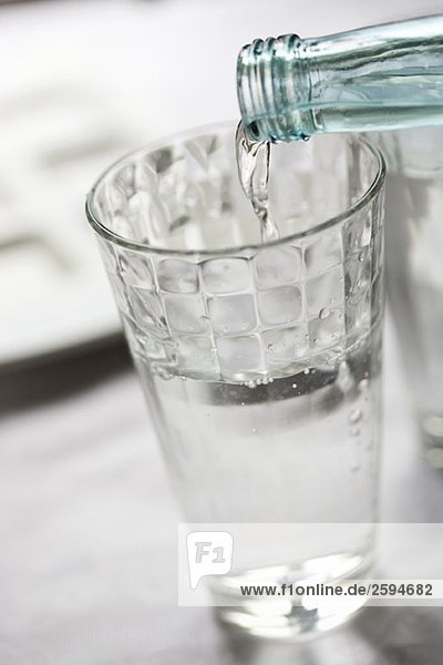 Flaschenwasser  das in ein Glas fließt.