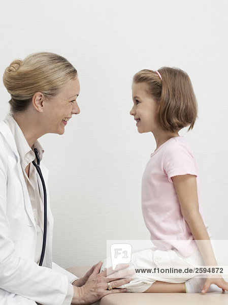 Ein Mädchen auf einem Untersuchungstisch mit Blick auf einen Kinderarzt und lächelndem Gesicht