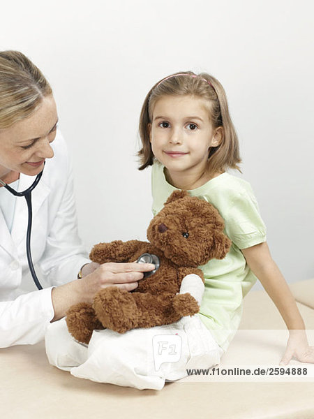 Eine Kinderärztin untersucht den Teddybär eines Mädchens.