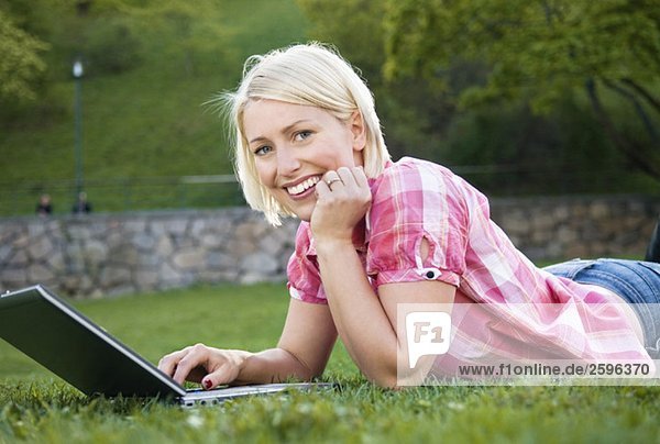 Girl on her belly in the park with a computer