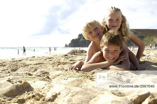 Portrait von drei Kindern am Strand liegen und lächelnd