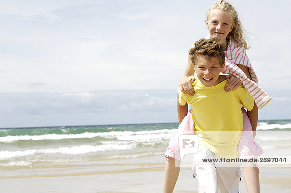 Porträt von Boy geben eine piggyback ritt zu seiner Schwester am Strand