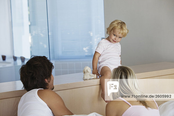 Junges Paar liegt in Bett Baby (12-24) sitzt an Bett und sieht Eltern an