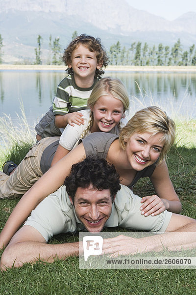 Family with two children lying on grass human pyramid in front of lake