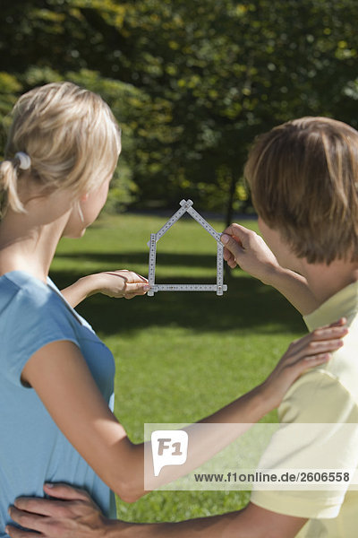 Junges Paar im Freien halten Meterstab in Form eines Hauses in der Hand
