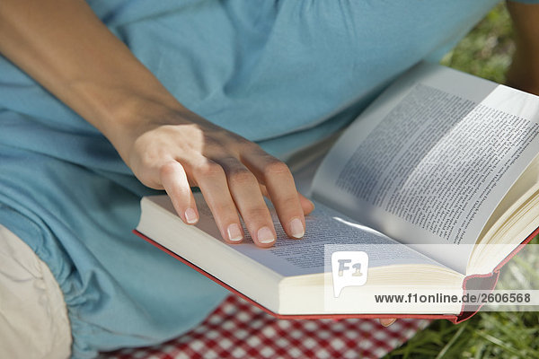 Frau liegt im Gras auf Decke ließt ein Buch