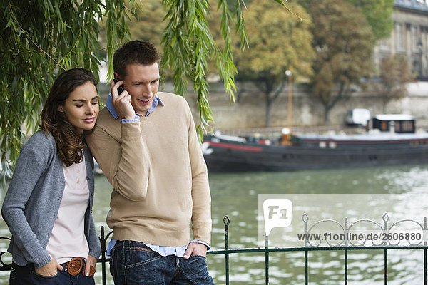 Young couple by river Seine man using mobile phone Paris France