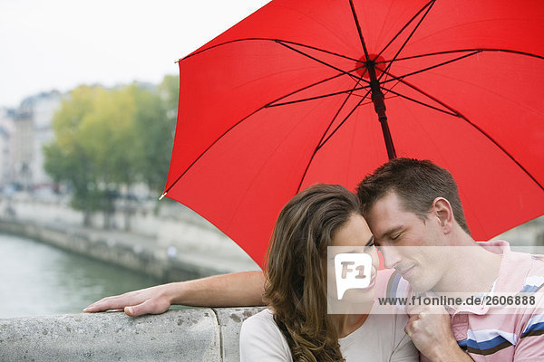 Junges Paar mit Regenschirm sitzt auf Steinbank an der Seine Paris Frankreich