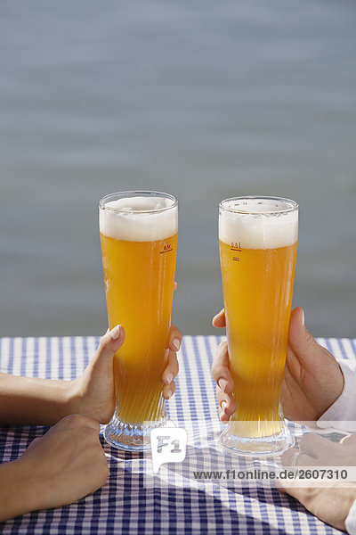 Junges Paar hält Weizenbiergläser in der Hand Biergarten am Seehaus Englischer Garten Nahaufnahme der Gläser und Hände