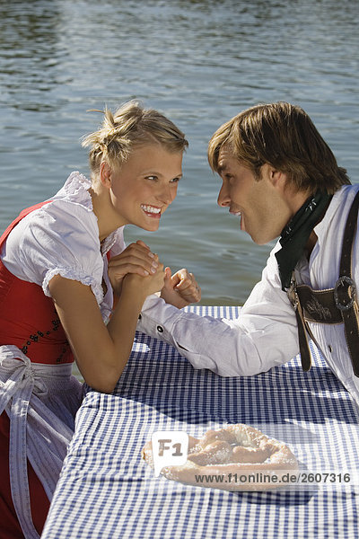 Junges Paar in Tracht sitzt am Biertisch mit Breze beim armdrücken Biergarten am Seehaus Englischer Garten Nahaufnahme