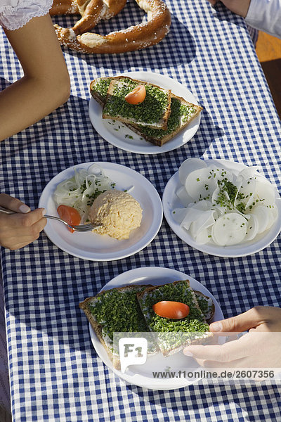 Junges Paar sitzt am Biertisch mit Schnittlauchbrote Radi Obatzda und Breze beim essen Biergarten am Seehaus Englischer Garten Nahaufnahme