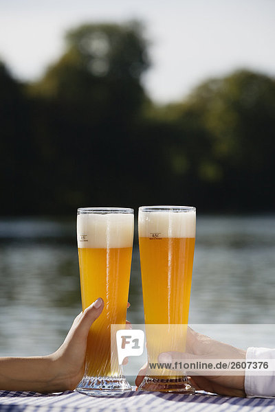 Junges Paar hält Weizenbiergläser in der Hand Biergarten am Seehaus Englischer Garten Nahaufnahme der Gläser und Hände