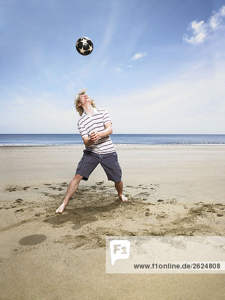 Junger Mann mit Fußball am Strand