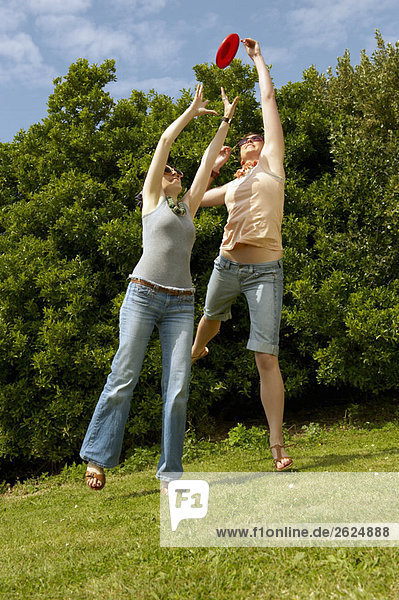 Zwei Frauen springen  um einen Frisbee zu fangen.