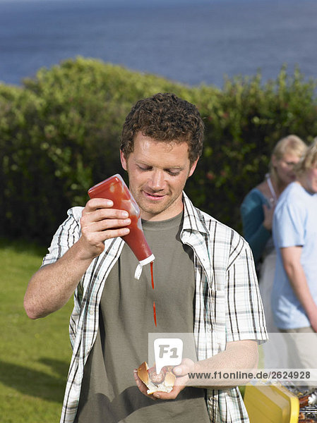 Mann gießt Ketchup auf Hot Dog