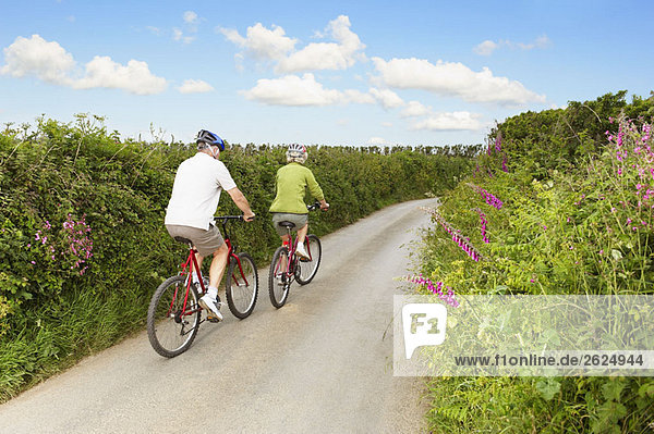 Senior couple cycling up country lane