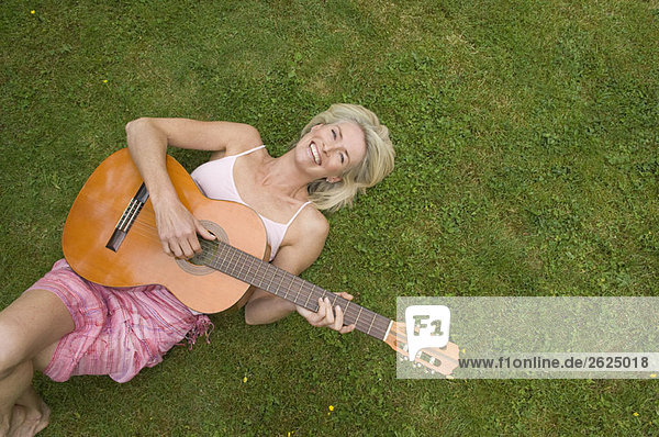 Frau auf Gras liegend  Gitarre spielend