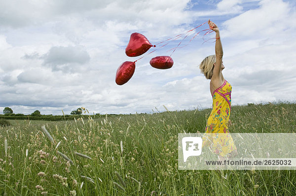 Frau geht mit Luftballons auf dem Feld spazieren