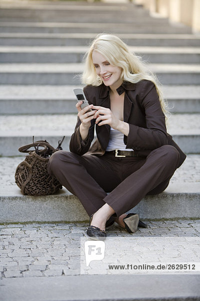 Junge Frau mit Handy  auf Stufen sitzend  Portrait