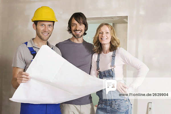 Young couple and construction worker holding construction plan  smiling  portrait