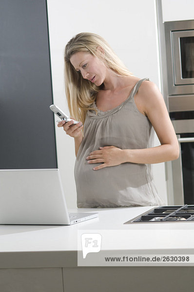 Schwangere Frau in der Küche liest SMS