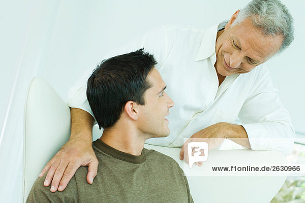 Man leaning over adult son's shoulder  both smiling at each other