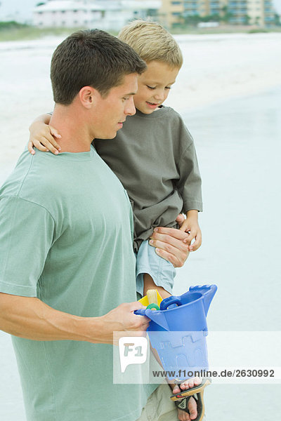 Vater mit Sohn am Strand  Plastikeimer in der Hand