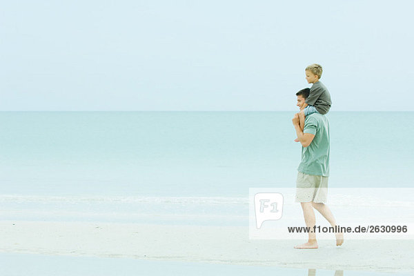 Vater trägt den Sohn auf den Schultern  läuft auf einem verlassenen Strand.