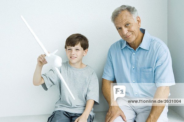 Grandfather sitting with grandson  smiling as grandson plays with toy airplane